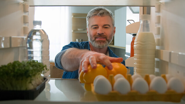 Point of view POV from inside refrigerator fridge middle-aged Caucasian man buyer customer unpack food delivery shopping bag with healthy meal in kitchen unpacking paper package vegetables products