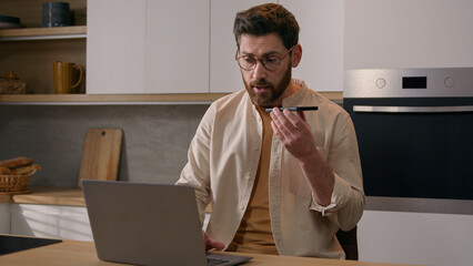Multitasking Caucasian man working with laptop recording dictating voice message voicemail with...
