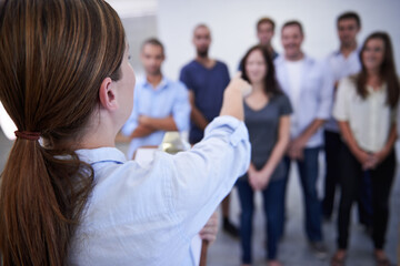 Woman, office and point at people for decision on training at work, back view and clipboard with...