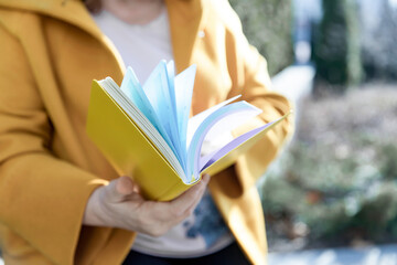 A woman in a yellow coat holds a flipping notebook - obrazy, fototapety, plakaty