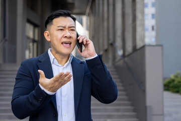 Frustrated businessman in suit gesturing while talking on smartphone outdoors