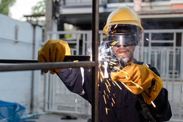 Asian worker wearing goggles, gloves, hat and safety suit uses a welding machine. Sparks from...