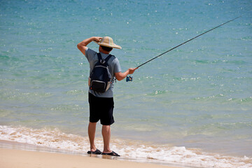 Fisherman standing with a fishing rod on a sea beach