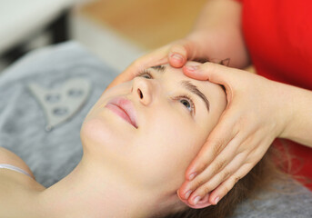 specialist gives a relaxing facial massage to a young woman patient. Facial care