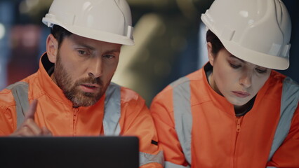 Focused engineers looking laptop checking production project on factory close up