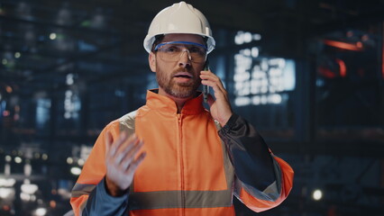 Professional craftsman talking cellphone at factory warehouse in uniform closeup - obrazy, fototapety, plakaty