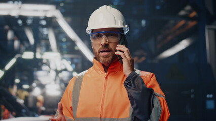 Nervous industrial worker talking smartphone solving problems at factory closeup