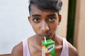 Portrait, teenager and drinking juice outdoor for healthy diet, wellness or nutrition in India. Face, boy and beverage with straw in box for benefits, energy and organic liquid fruit for hydration