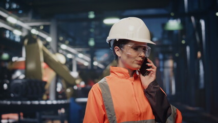 Worried engineer calling cellphone at workshop in protective helmet close up.