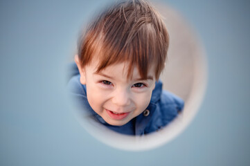 A charming toddler peeks through a playground tunnel, highlighting the curiosity and delight of a...
