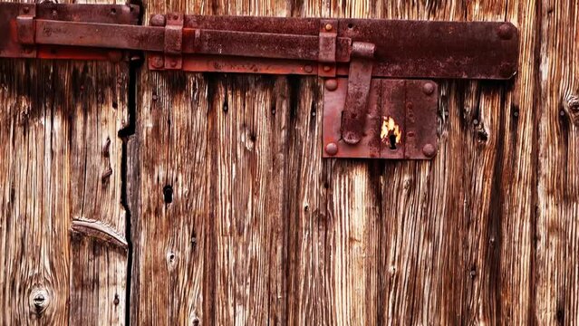 An old wooden door with a hinged vintage iron bolt. Rusty massive iron lock on an abandoned wooden gate. Sun-faded, aged and bark beetle-eaten wooden doors. Rovinj, Croatia - February 29, 2024