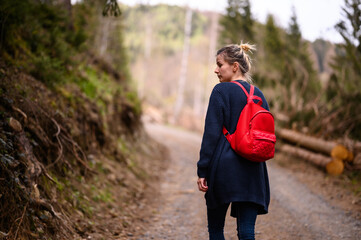 A thoughtful woman with a red backpack enjoys a moment of peace on a forest trail, surrounded by the tranquil beauty of nature
