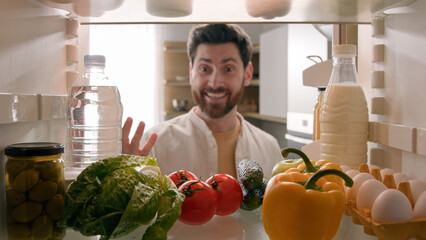 Point of view POV inside refrigerator happy excited hungry Caucasian man open fridge full of...