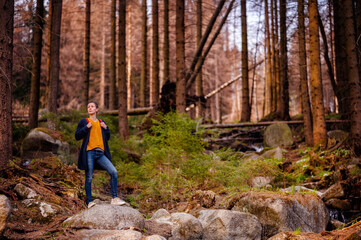 A hiker stands atop a stone, surrounded by the tranquil beauty of a forest, absorbing the serenity of the natural world