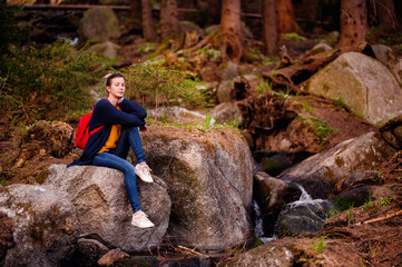 Amidst a rustic forest setting, a young woman finds a moment of reflection while seated on a...