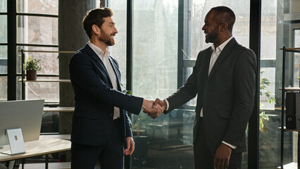 Two diverse men multiracial businessmen talking in office shake hands after successful...