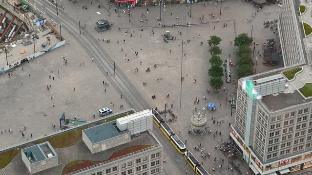 Berlin, Germany, August 15, 2023. Aerial view footage: In Alexanderplatz the moving people look like an anthill, a yellow and white tram crosses the square.
