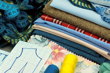 Sewing process. Stack of different fabrics and patterns close-up. Sewing accessories and fabric for sewing clothes.