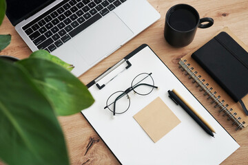Workplace with open laptop, notepads, folders, pen, glasses, calendar and black mug with coffee