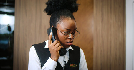 Attractive African-American female receptionist receiving calls talking on phone. Friendly young...