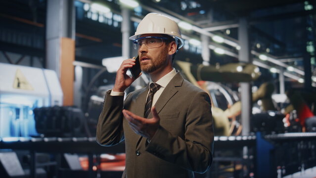 Serious factory owner calling smartphone at production in helmet close up.