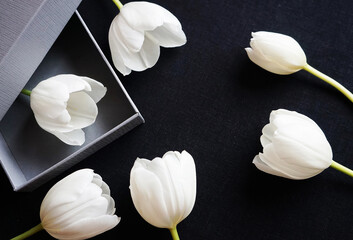 White tulips next to a gray gift box on a dark background