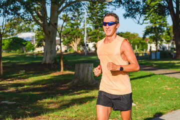 Young man dressed in sportswear runs during training in the park between eucalyptus trees, summer sunny day.