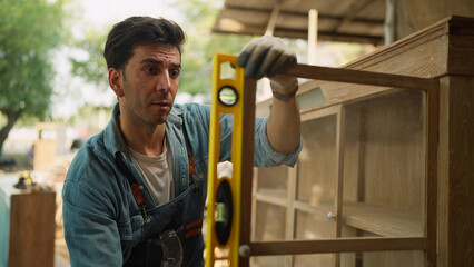 A male carpenter using precision level making new furniture at wood workshop. Carpenter using...