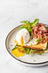 Toasts sandwich with poached egg, arugula, bacon and cream cheese on white plate marble background. Isolated, text space