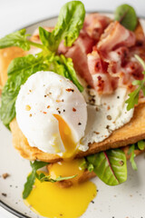 Toasts sandwich with poached egg, arugula, bacon and cream cheese close up on white plate