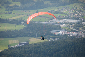 A Red Paraglider Soaring in the Sky Above a Forest