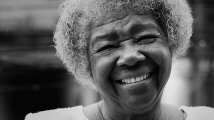 One joyful older black woman with friendly charismatic expression smiling at camera while standing...