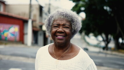 One mature black senior woman walking in city street outside. African American elderly lady in 80s...