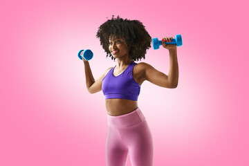 Fototapeta na wymiar Smiling woman with dumbbells raised, wearing a purple sports bra and leggings against gradient pink studio background. Concept of sport, mourning routine, active and healthy lifestyle, energy, action.