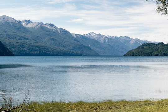 Tranquil waters of a Patagonian lake reflect the surrounding mountain range and lush forests under a clear blue sky