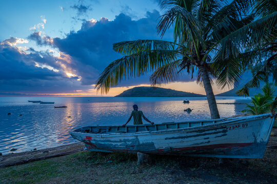 View of local man sat on boat viewing Le Morne from Le Morne Brabant at sunset, Savanne District, Mauritius