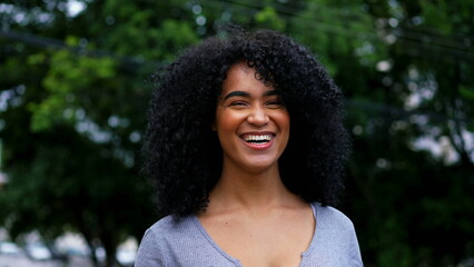 One happy Brazilian young black woman smiling and laughing while posing for camera outside in city...