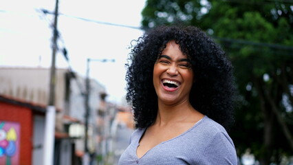 One happy Brazilian young black woman smiling and laughing while posing for camera outside in city...