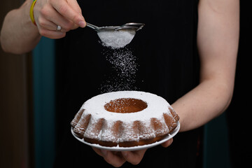 Ciasto cytrynowe w formie babki z dziurką w trakcie posypywania cukrem pudrem z bliska - obrazy, fototapety, plakaty