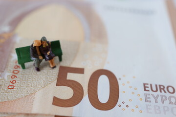 Retired micro people, sitting down on a bench, on a Euro paper money.