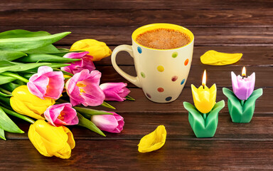 Fototapeta na wymiar Spring still life with a white polka dot cup of coffee, a bouquet of yellow and pink tulip flowers and a candles on a wooden background.
