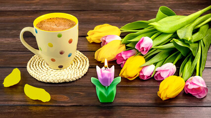 Spring still life with a white polka dot cup of coffee, a bouquet of yellow and pink tulip flowers and a candle on a wooden background.