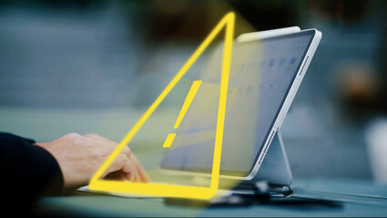 person working on a tablet computer, yellow warning triangle as an alert of spam or malware...