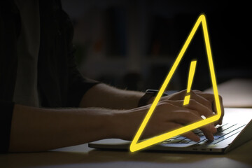 person working on a laptop computer, yellow warning triangle as an alert of spam or malware...