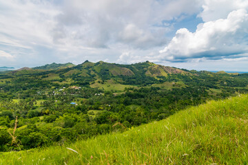 Fototapeta na wymiar A picturesque view of Mabini, Bohol featuring rolling green hills, tropical vegetation, and a serene sky.