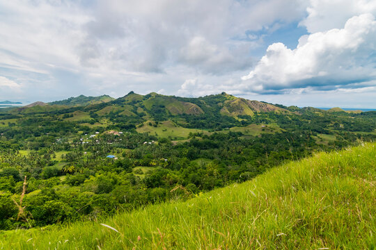 A picturesque view of Mabini, Bohol featuring rolling green hills, tropical vegetation, and a serene sky.