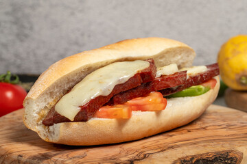 Turkish bread sandwich with kashar sausage on the presentation board. Sausage in bread prepared with tomatoes, peppers and meatballs. Local name ekmek arası sucuk