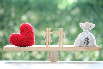 Love couple with heart shape and money bag on wood scale seesaw on natural green background