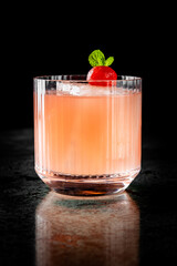 A vibrant pink cocktail adorned with a red cherry and mint leaf, served in a clear glass against a...