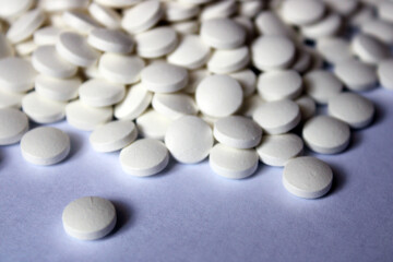 A lot of white pills are scattered on a white background.
